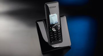 Ein schwarzes schnurloses Telefon steht in seiner Ladestation auf glänzender Oberfläche.